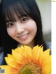 A woman holding a sunflower in front of her face.