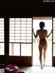 A naked woman standing in front of a sliding glass door.