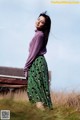 A woman in a purple sweater and green skirt standing in a field.