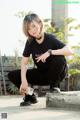 A woman in a black shirt and black pants crouching on a concrete ledge.