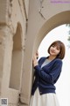 A woman leaning against a wall wearing a blue cardigan.