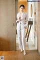 A woman in a white suit standing in a hallway.