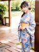 A woman in a blue kimono standing on a wooden deck.