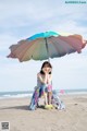 A woman sitting on a beach under an umbrella.